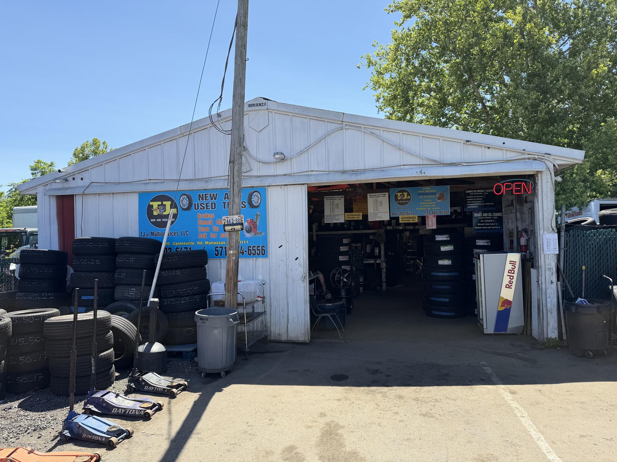TJ Jr storefront — white building with the red OPEN neon, blue sign and tire stacks out front