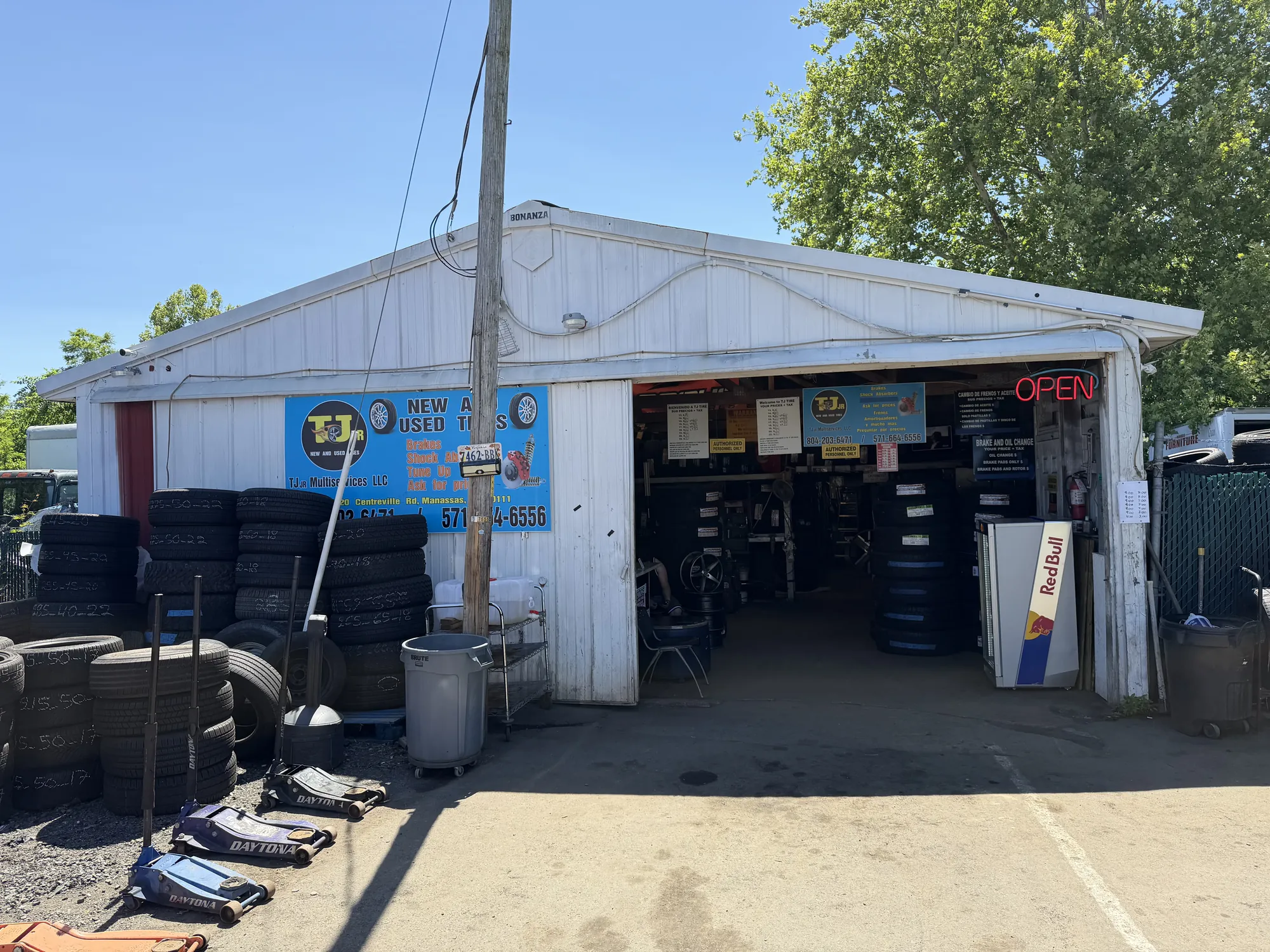 TJ Jr New & Used Tires storefront on Centreville Rd in Manassas, VA — white building with red OPEN neon sign and stacks of tires