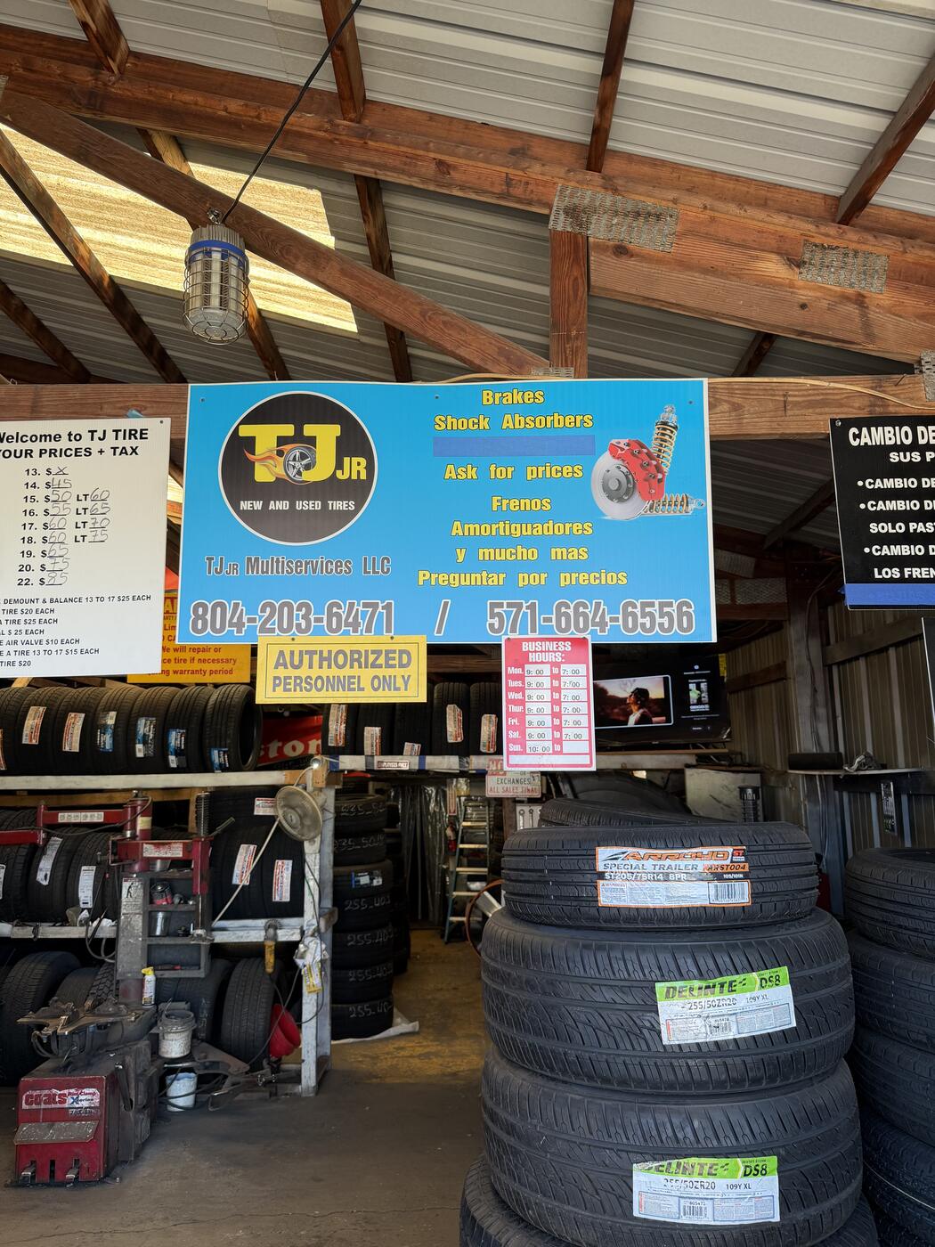 Inside the TJ Jr shop — bilingual blue service sign listing brakes, shock absorbers and 'frenos, amortiguadores' above racks of new tires