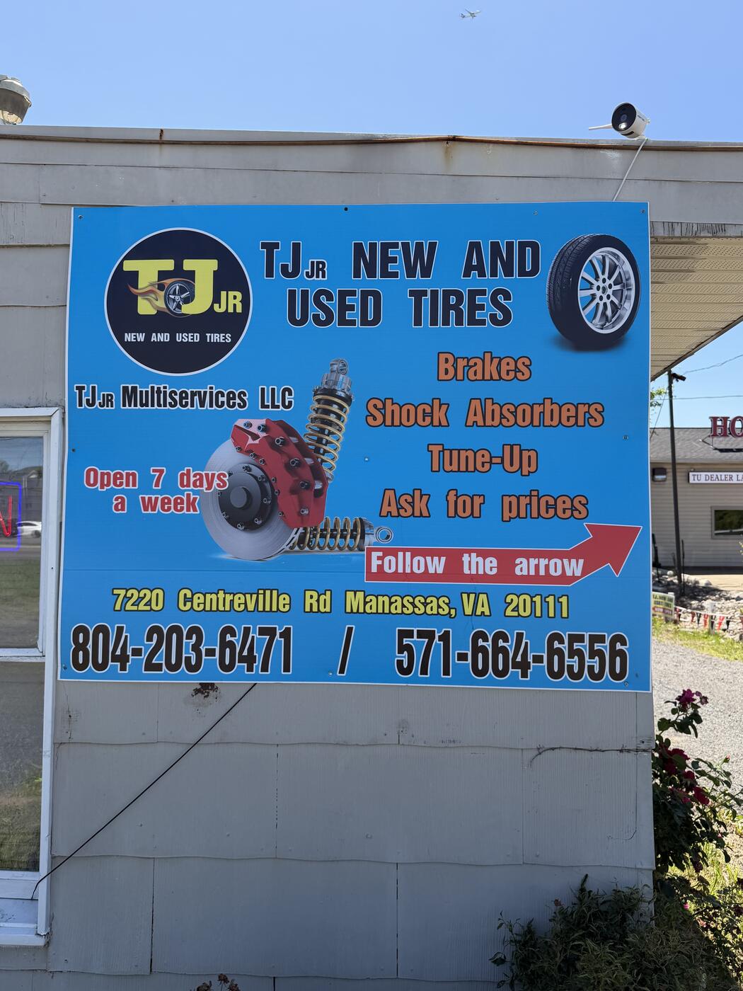 The big blue TJ Jr roadside sign — 'TJ Jr New and Used Tires, Brakes, Shock Absorbers, Tune-Up, Ask for prices, Follow the arrow', 7220 Centreville Rd Manassas VA, phones 804-203-6471 / 571-664-6556
