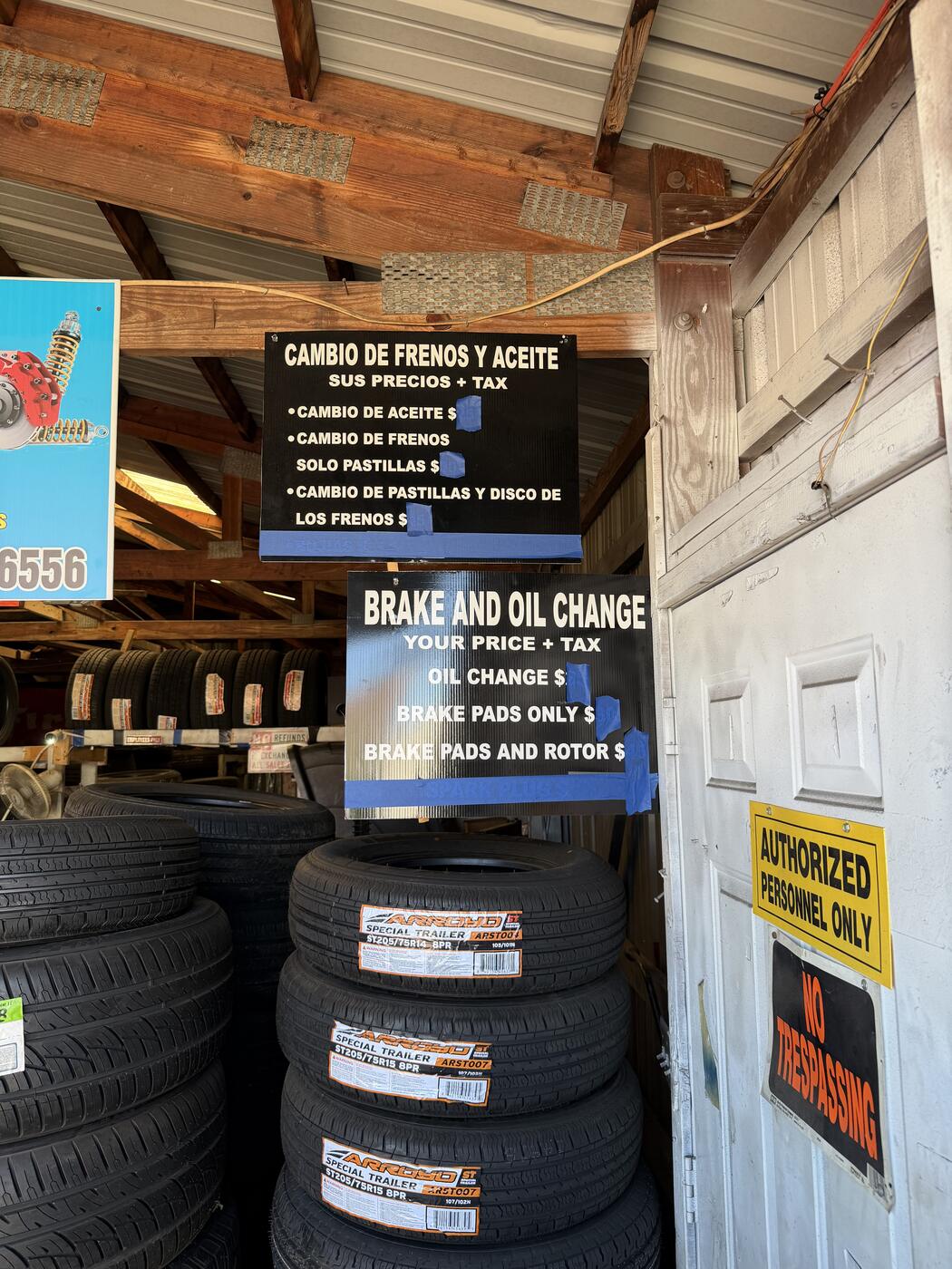 Bilingual price boards at TJ Jr — 'Brake and Oil Change / Cambio de Frenos y Aceite — Your Price + Tax' above stacked tires